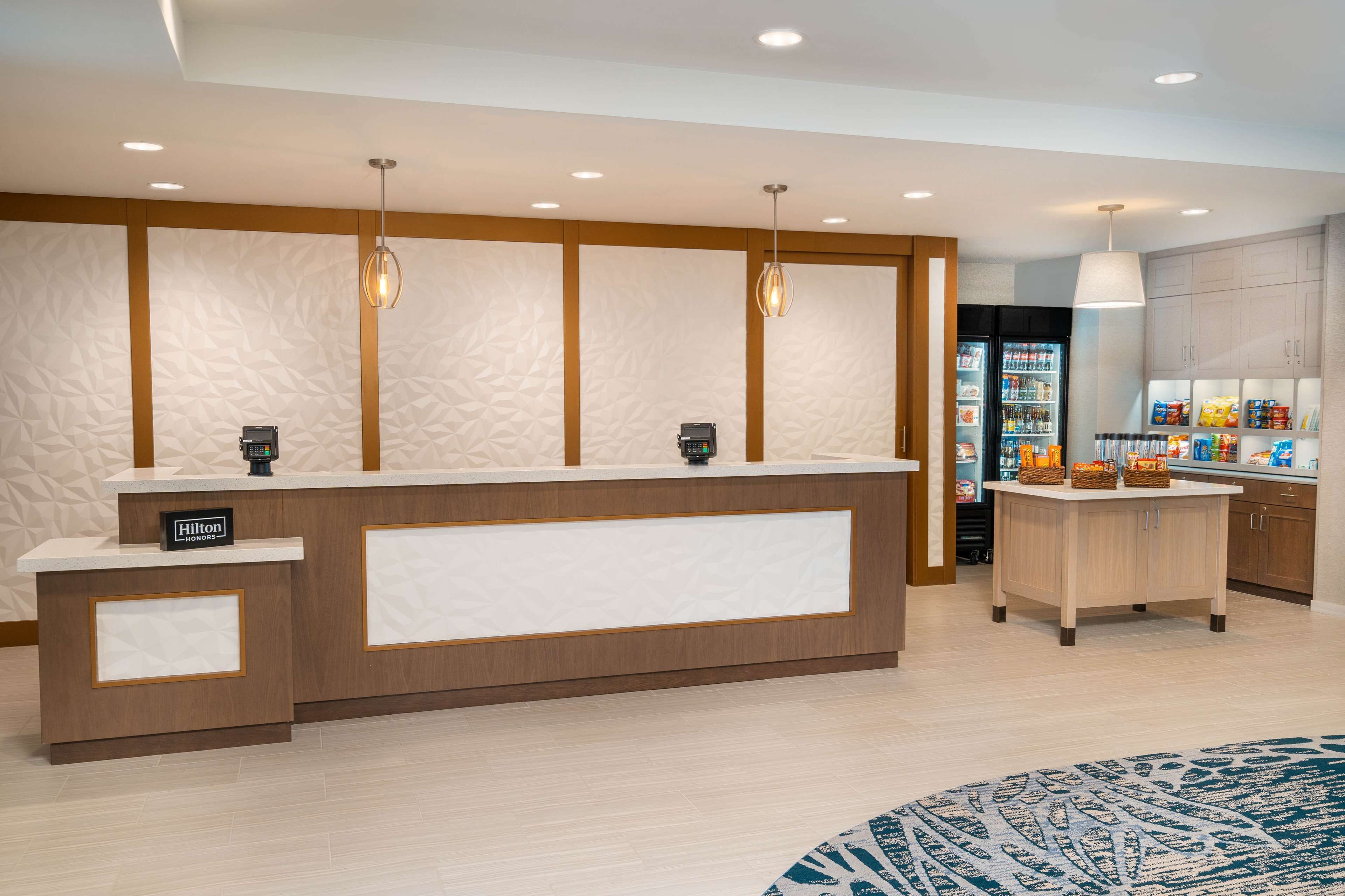 Un espace d’accueil d’hôtel au design moderne, comprenant un comptoir de réception, un minibar et un réfrigérateur rempli de collations.