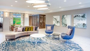Un vestíbulo moderno con un sofá modular, un sillón azul, una mesa de centro redonda y arte abstracto en la pared.
