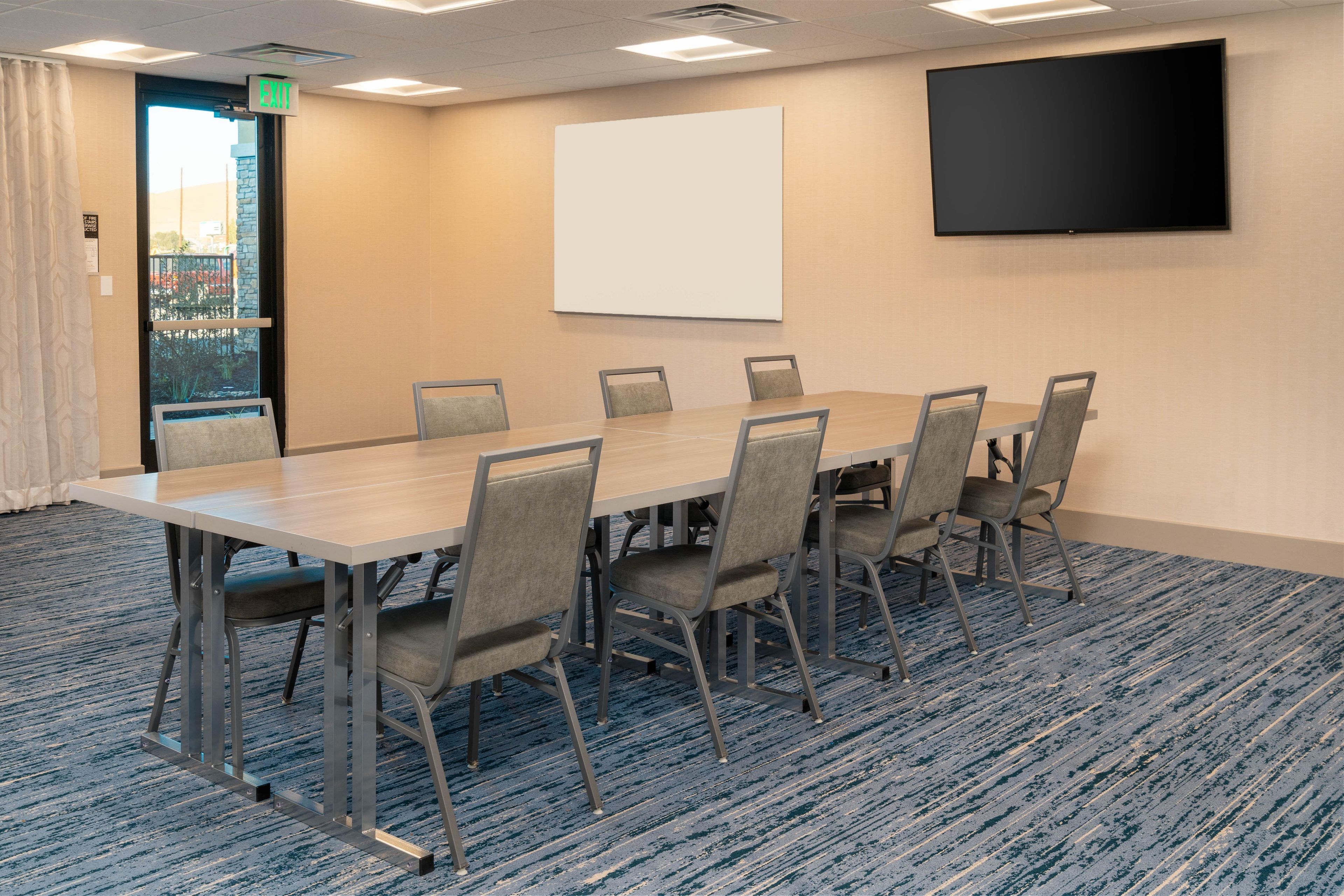 A conference room with a long table, six chairs, a projector screen, and a TV on the wall.