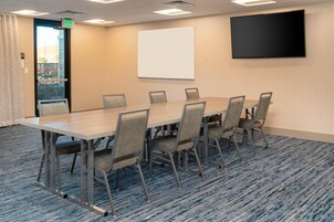 Un salón de conferencias con una larga mesa, seis sillas, una pantalla de proyector y un televisor en la pared.
