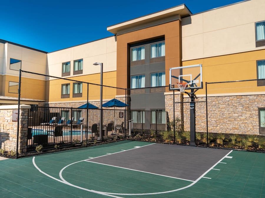 Ein Basketballplatz im Freien neben einem Gebäude mit Schwimmbad und Liegestühlen.