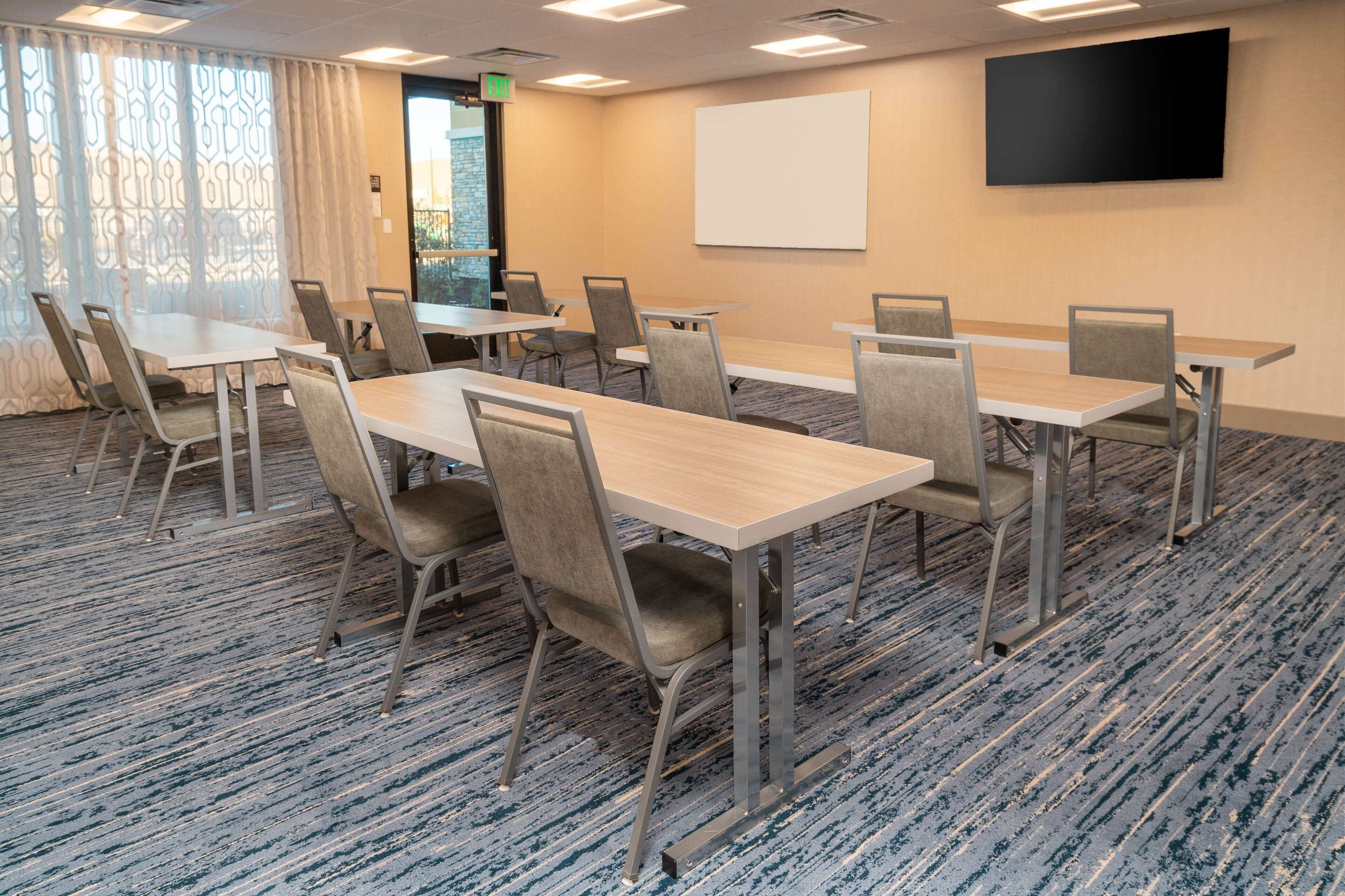 A conference room with six tables and chairs, a projector screen, and a patterned curtain.