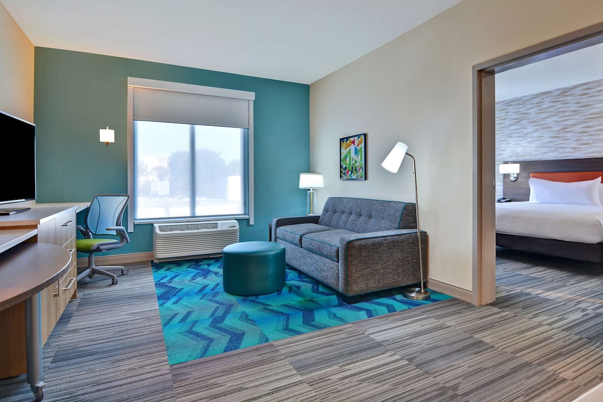Une chambre d’hôtel équipée d’un bureau, d’une chaise, d’un canapé, d’un pouf et d’un lit.