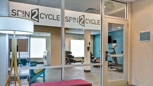Une salle de sport avec un banc d’exercice rouge, un tapis de course et un téléviseur fixé au mur.