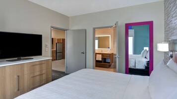 Quarto de hotel com uma cama grande, televisão de tela plana, armários de madeira, banheiro com espelho e porta que dá para outro quarto.