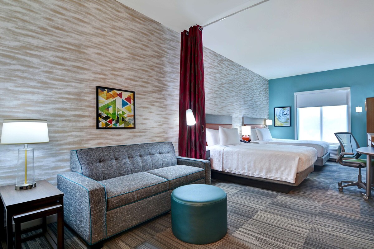 Ein Hotelzimmer mit Sofa, Bett, Schreibtisch, Stuhl, Lampe und einem Bild an der Wand.