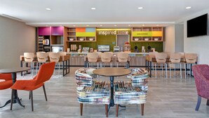 Un restaurant moderne doté d’une salle à manger centrale, avec des tables rondes et des chaises aux couleurs vives.