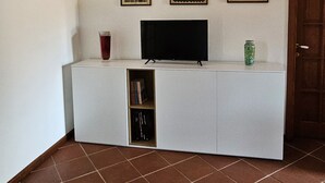 Un petit espace de vie compact, avec un téléviseur à écran plat posé sur un meuble blanc, une porte et trois tableaux encadrés accrochés au mur.
