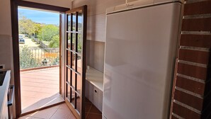 Une cuisine équipée d’un réfrigérateur, d’une fenêtre et d’une porte donnant sur un balcon.