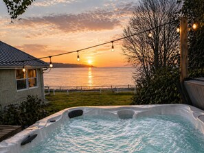 A hot tub with a sunset view, a house, and string lights. - Beachfront Retreat with Hot Tub, Kayaks & Fire pit (Clinton)