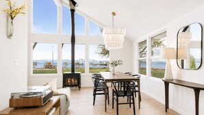 Una sala de estar moderna con chimenea, ventanas amplias, zona de comedor y vistas al exterior.