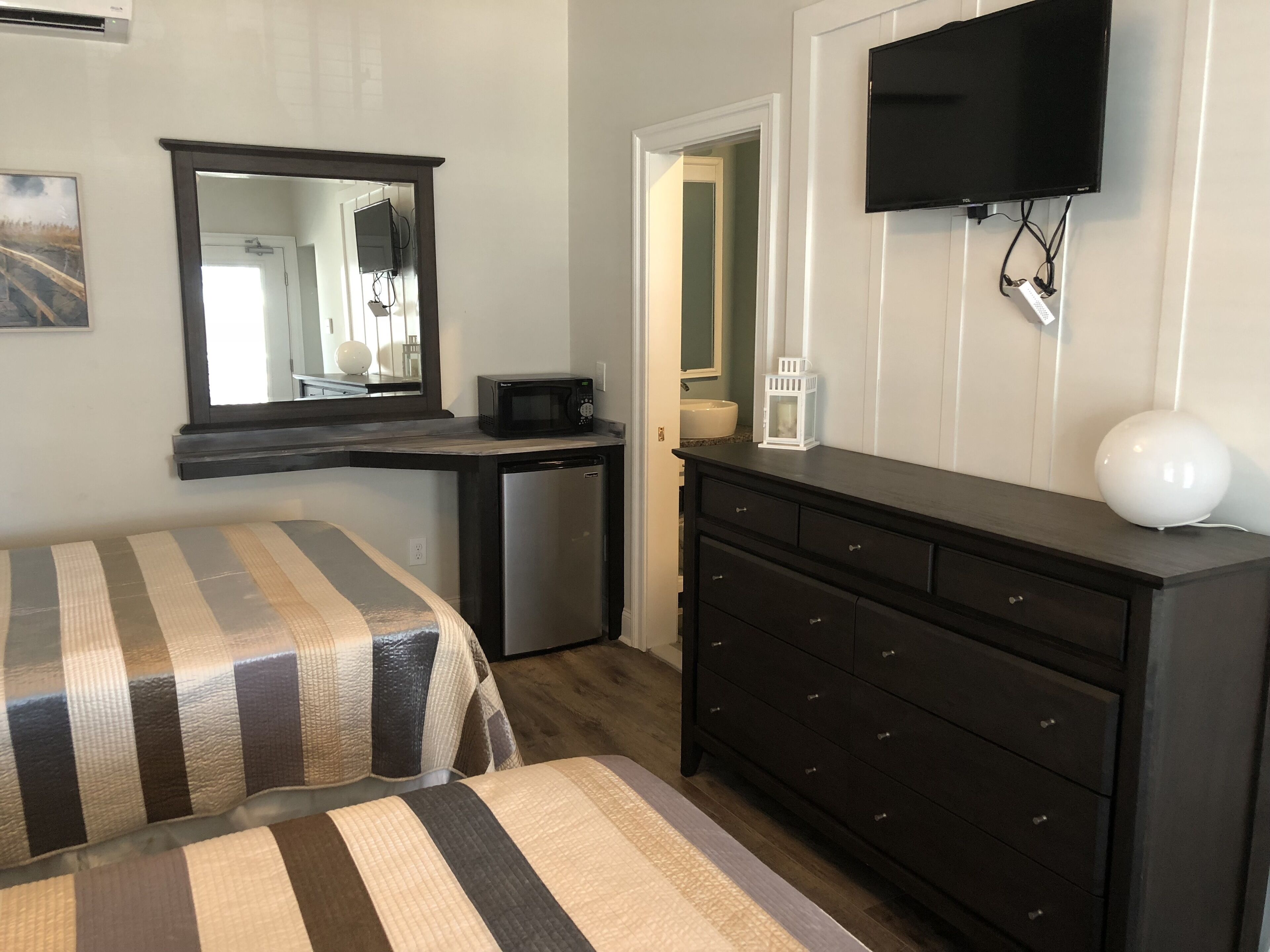 A bedroom with a bed, a dresser, a television, and a microwave.