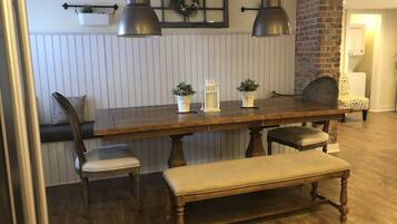 A dining area with a wooden table, two chairs, a bench, and pendant lights.