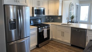 Una cocina moderna con electrodomésticos de acero inoxidable, armarios blancos y piso de madera.