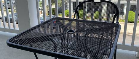 Un balcon avec une table et des chaises en métal, donnant sur un quartier résidentiel avec des maisons et une rue.