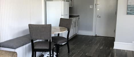 Een ruimtelijke woonkamer met een eethoek, een kitchenette en een deur naar een andere kamer.