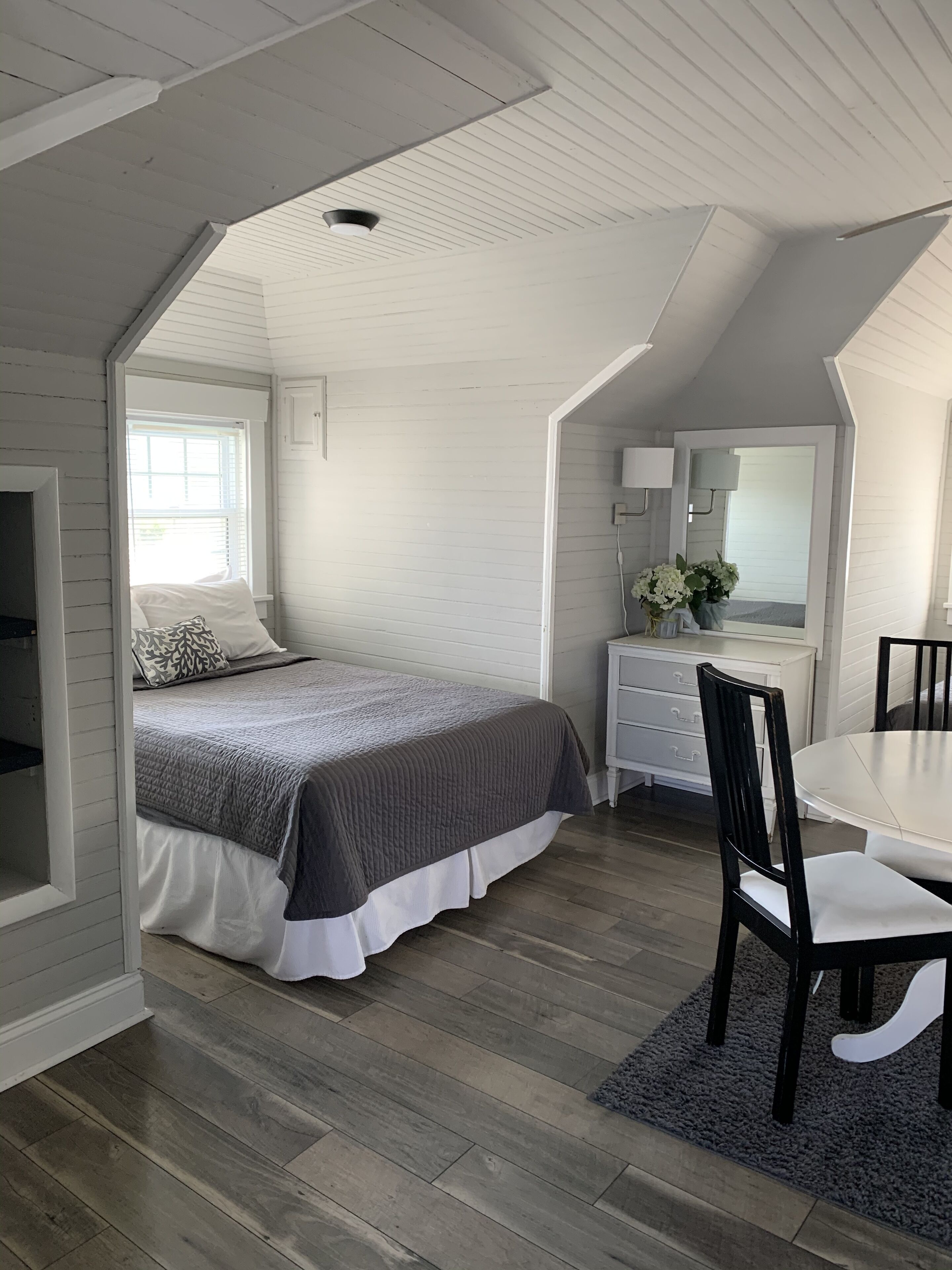 Ein Schlafzimmer mit Bett, Kommode, Spiegel und Esstisch.