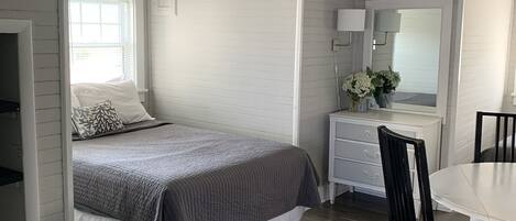 Ein Schlafzimmer mit Bett, Kommode, Spiegel und Esstisch.