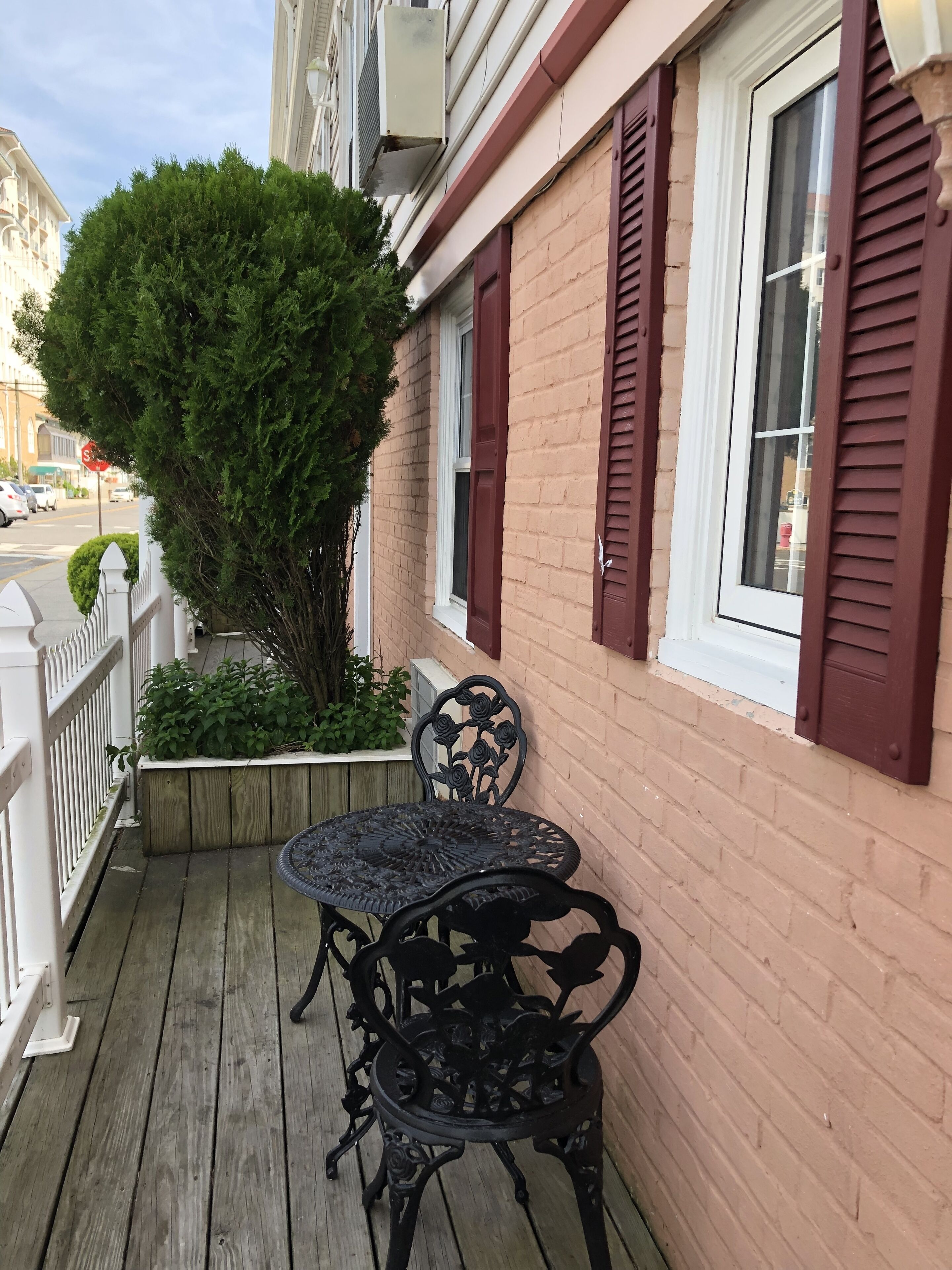 A wooden deck with a wrought iron table and chairs, a brick wall, and a window with shutters.