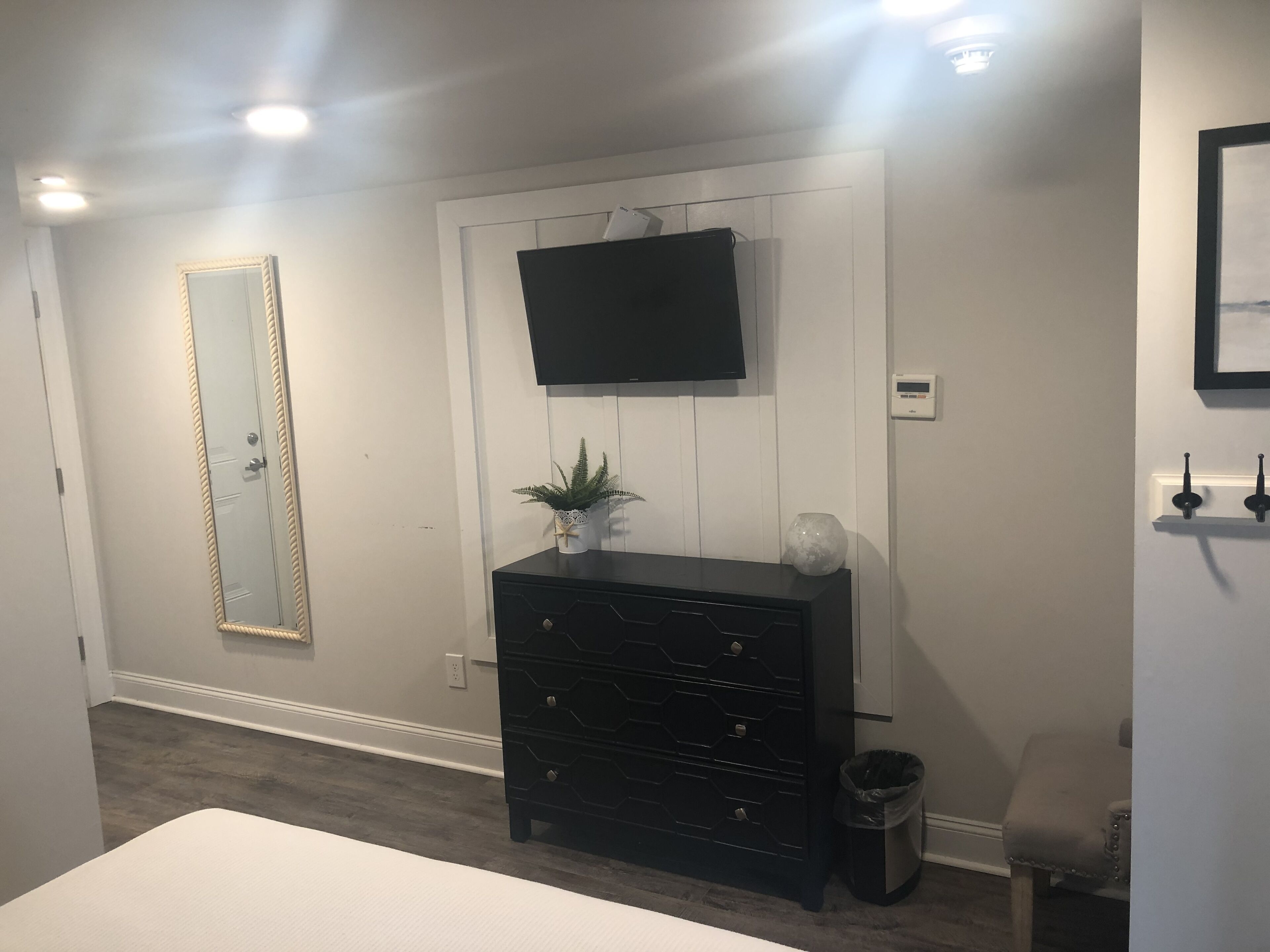 A bedroom with a bed, a dresser, a TV mounted on the wall, a mirror, and a thermostat.