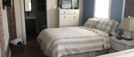 Un dormitorio con una cama doble, una mesita de noche, un aparador y una ventana.