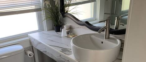 Un baño con inodoro blanco, lavabo con encimera de mármol y espejo sobre el lavabo.