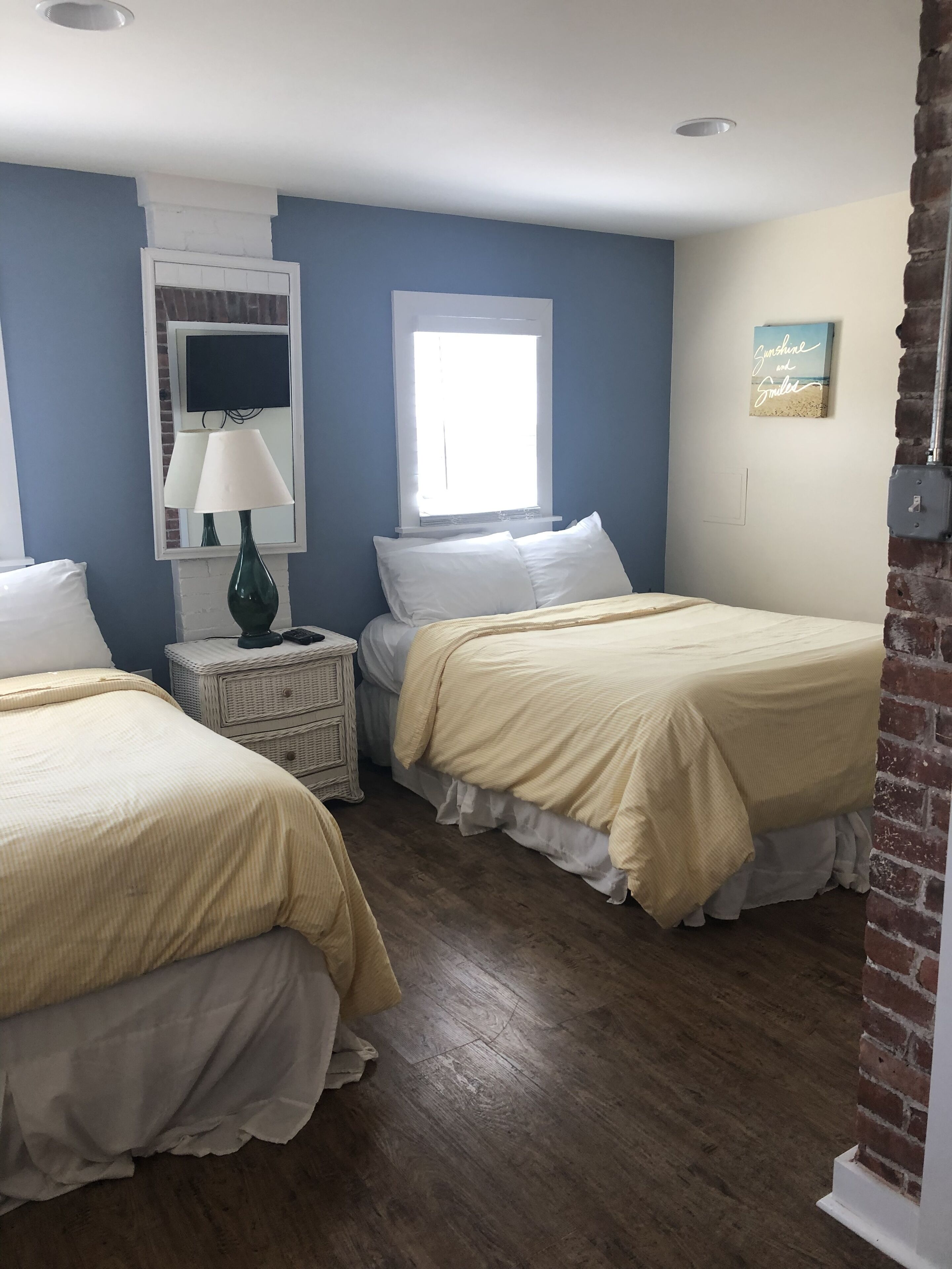 A room with two beds, a window, a lamp, and a wall-mounted TV.