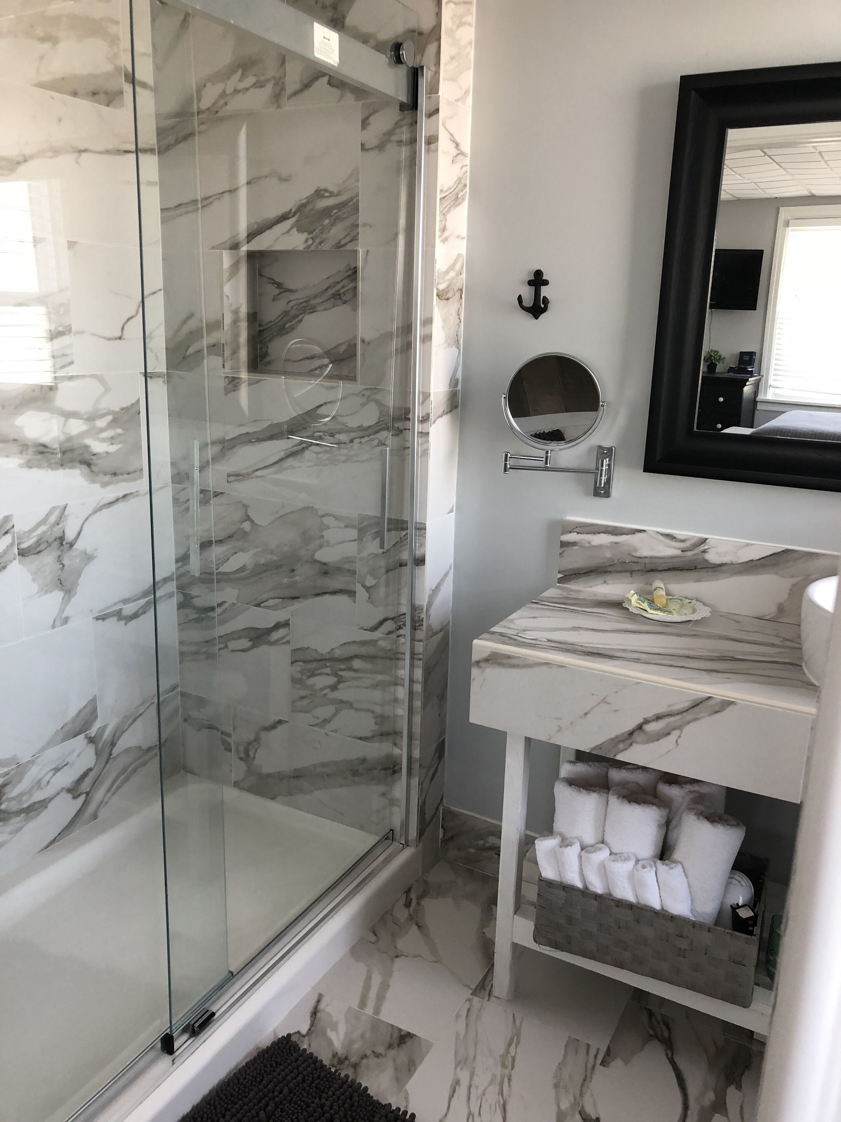 A bathroom with a glass-enclosed shower, a marble-tiled floor, a sink with a mirror, and a towel rack.
