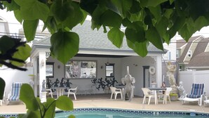 Zona de piscina con sillones de descanso y una mesa de comedor, rodeada de vegetación.