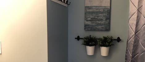A bathroom with a toilet, a roll of toilet paper, a wall-mounted rack with hooks, and two potted plants.