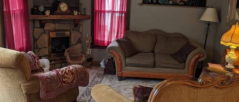A living room with a stone fireplace, two sofas, a television, and a ceiling fan.
