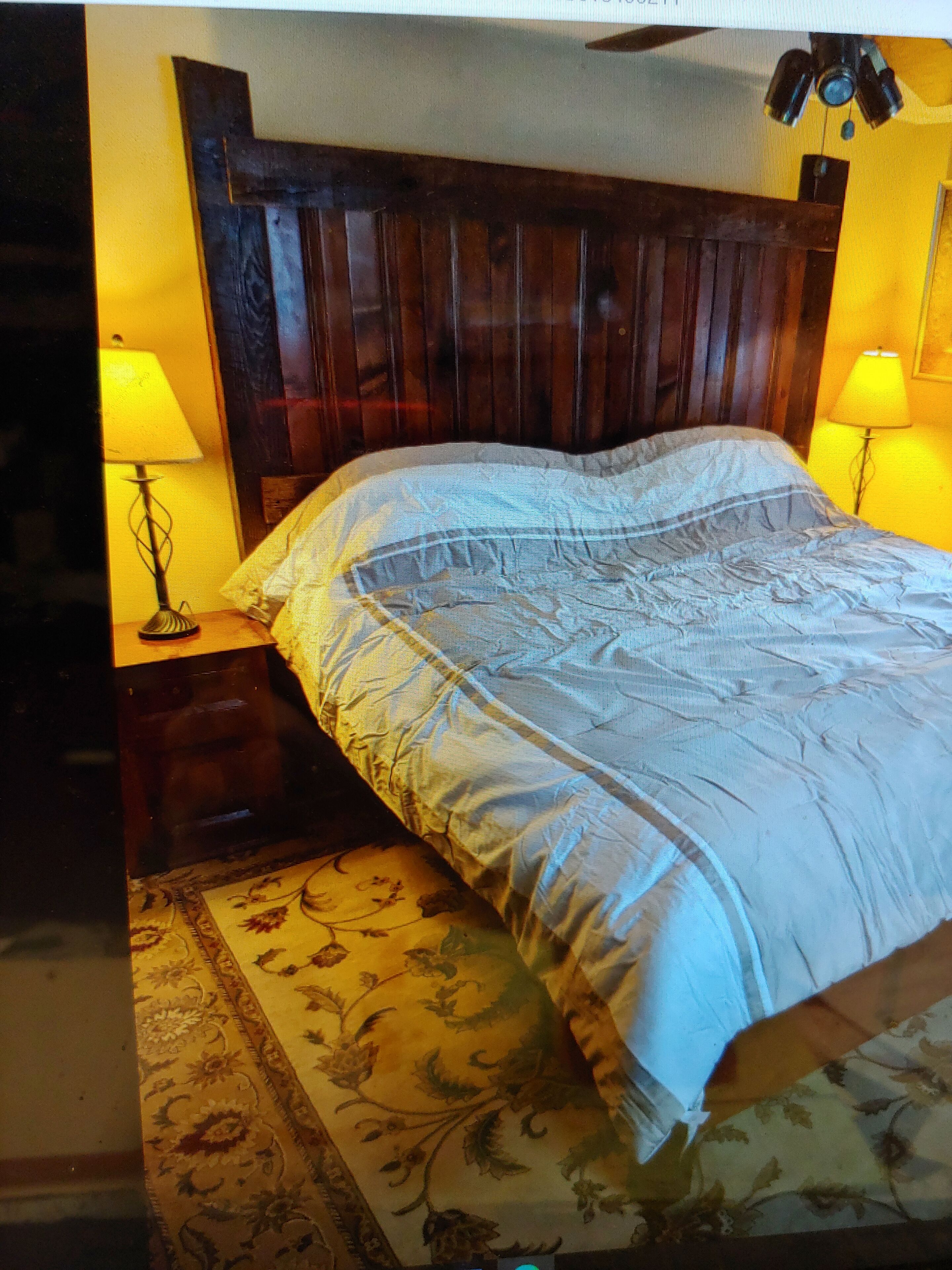 A room with a wooden headboard, a bed with a patterned bedspread, two bedside lamps, and a floral rug.