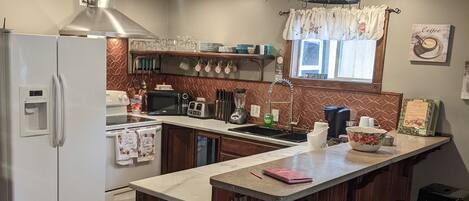 A kitchen with a central island, bar stools, a refrigerator, and a trash bin.