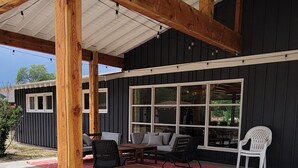 Ein überdachter Patio-Bereich mit Holzbalken, Gartenmöbeln und großen Fenstern.