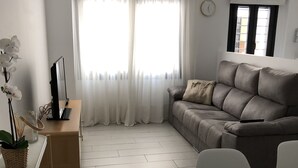 A modern living room with a grey sofa, white curtains, a wooden floor, and a dining area with a white table and chairs. - Fuengirola, 1 min. walk from the beach  (Fuengirola)