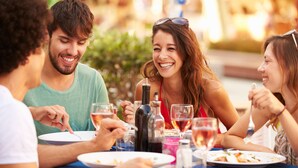 Un grupo de personas cenando en una mesa al aire libre, con diversos platos y bebidas.