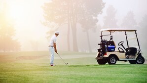Ein Golfplatz mit einem Spieler, der einen Ball vorbereitet, und einem Golfwagen in der Nähe.