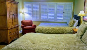 Un dormitorio con dos camas, un armario de madera, un sillón rojo y una mesita de noche con lámpara.
