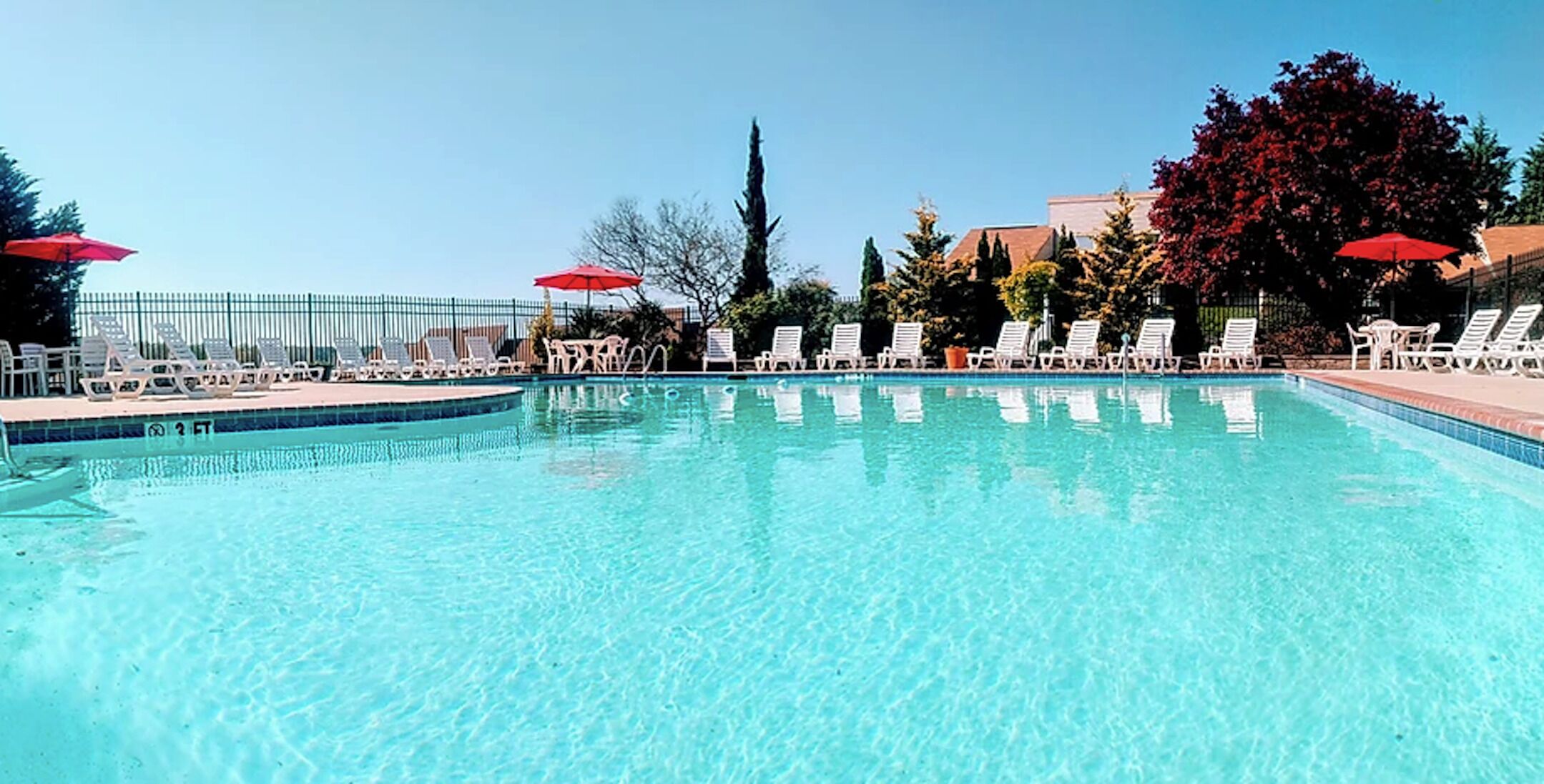 Una piscina cristalina con sillas de descanso blancas y sombrillas rojas.