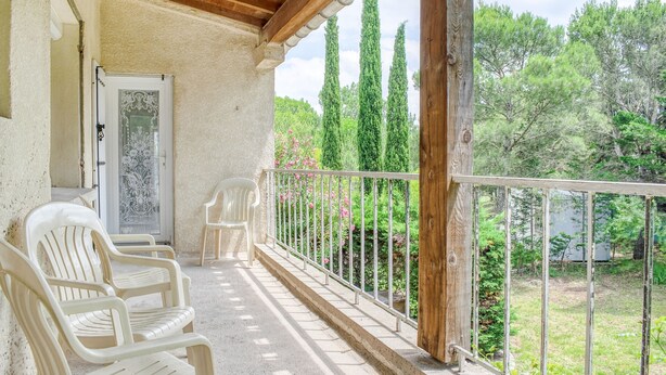 Un balcón con sillas de plástico blanco, techo de madera y vistas a zonas verdes y árboles.
