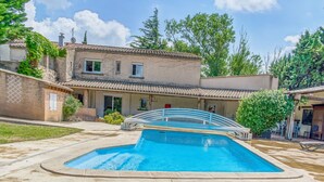 Una propiedad residencial con piscina, un patio cubierto y una casa de dos pisos con techo de tejas.