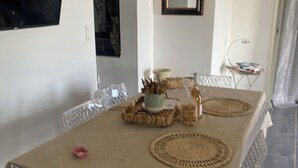 A dining area with a table covered in a beige cloth, surrounded by clear plastic chairs. A small pink object is on the table. - Ground floor apartment, T2 type, sea view. (Santa-Reparata-Di-Balagna)