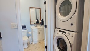 Ein Waschraum mit einer Frontlader-Waschmaschine und einem Trockner, ein Badezimmer mit Toilette, Waschbecken und Spiegel sowie Holzboden.