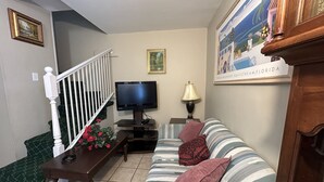 Un salon avec un téléviseur, un canapé, une table ornée de fleurs et un escalier.