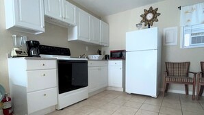 Une cuisine avec des armoires blanches, une cuisinière, un four à micro-ondes et un réfrigérateur. Un extincteur se trouve près de la cuisinière.