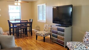 A living room with a dining table, chairs, a sofa, a TV, and a storage unit with suitcases. - Lakeview Cottage Near Boat Ramp (Burnet)