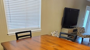 A dining area with a wooden table and chairs, a television, and a patterned armchair. - Lakeview Cottage Near Boat Ramp (Burnet)