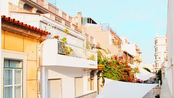 A narrow street with buildings on both sides, featuring balconies with plants and railings.