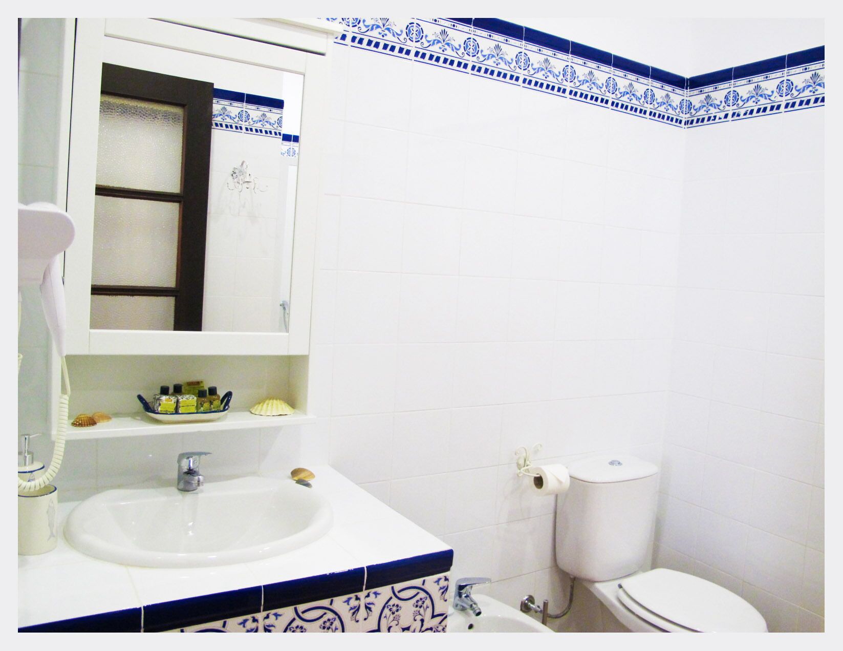 A bathroom with a white sink, a mirror, a toilet, and a shelf with toiletries.