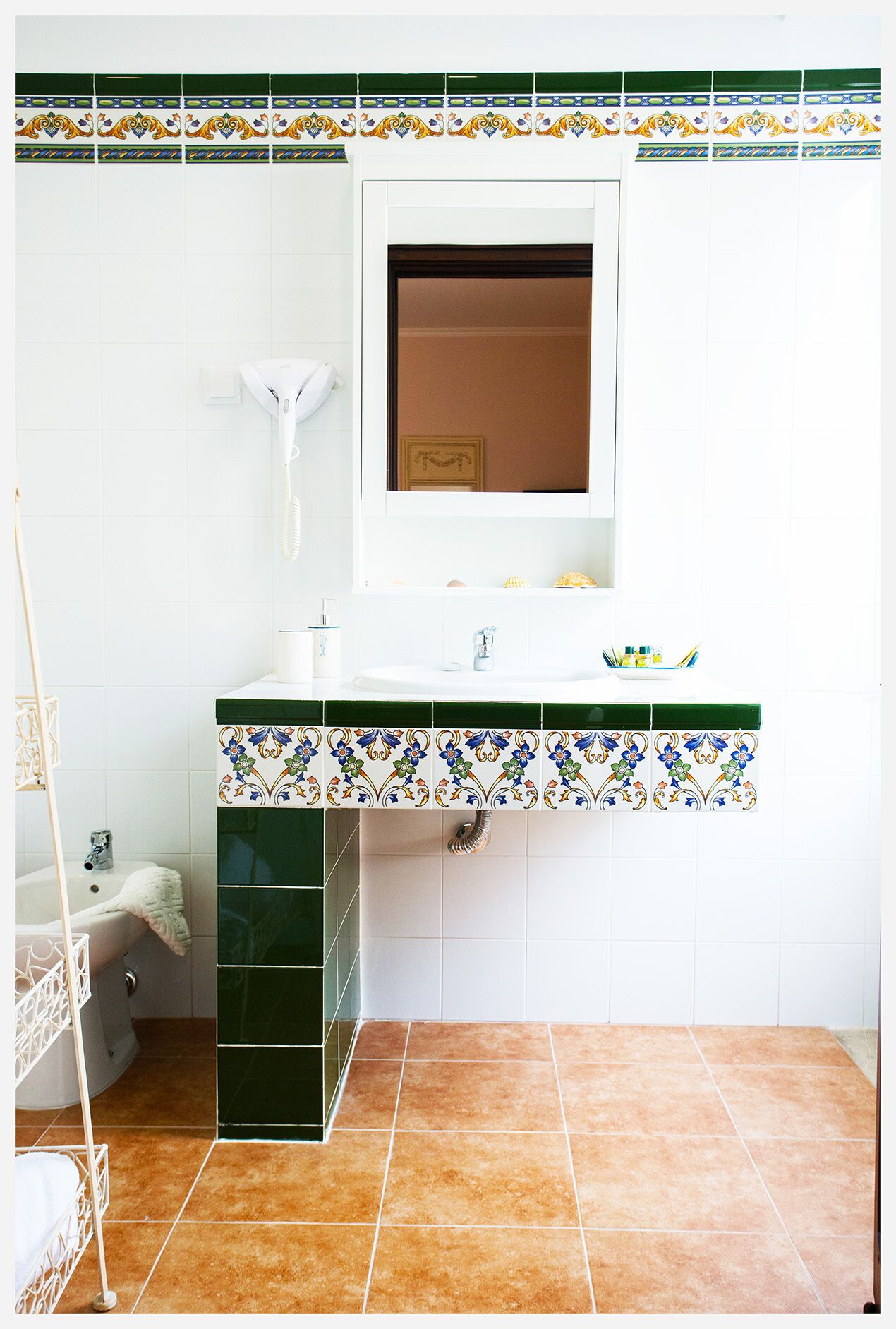 Un baño con lavamanos blanco, azulejos verdes, un espejo y un perchero para toallas.